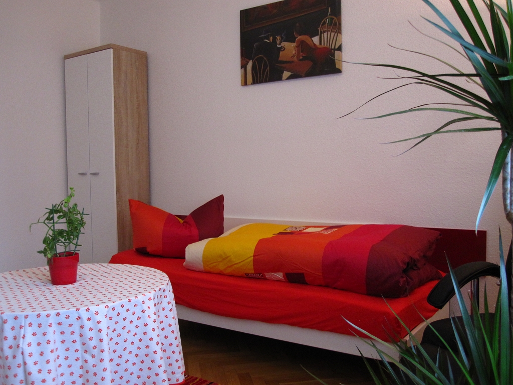 Einzelschlafzimmer Mit Bett, Kleiderschrank, Tisch Und Wandbild Sowie Großer Zimmerpflanze